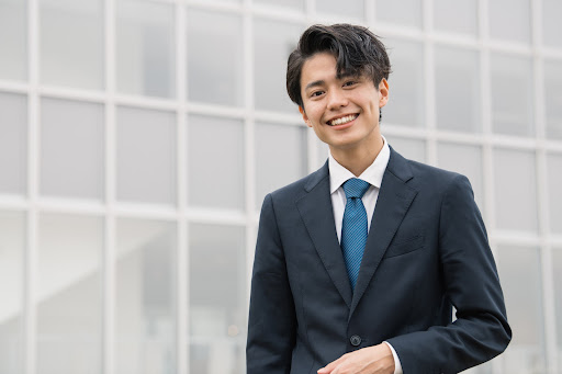 20代男性のビジネスパーソンが笑顔でこちらを見ている様子