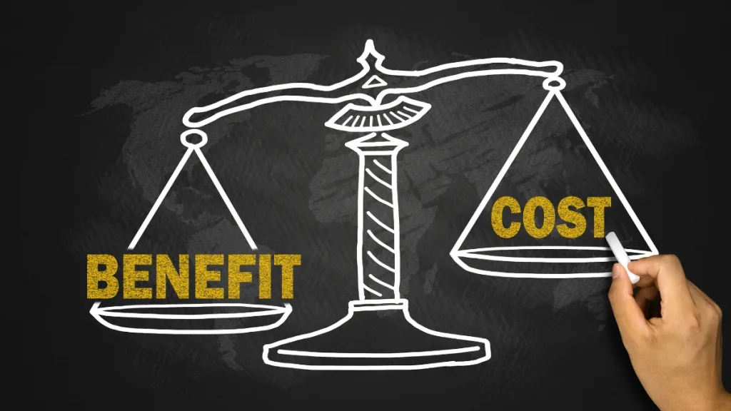 黒板に白い天秤の上にCOSTとBENEFITの文字を書いている