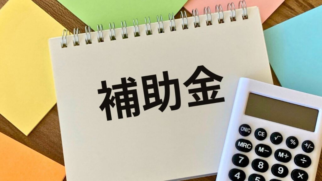 ノートに補助金の文字と電卓と付箋紙