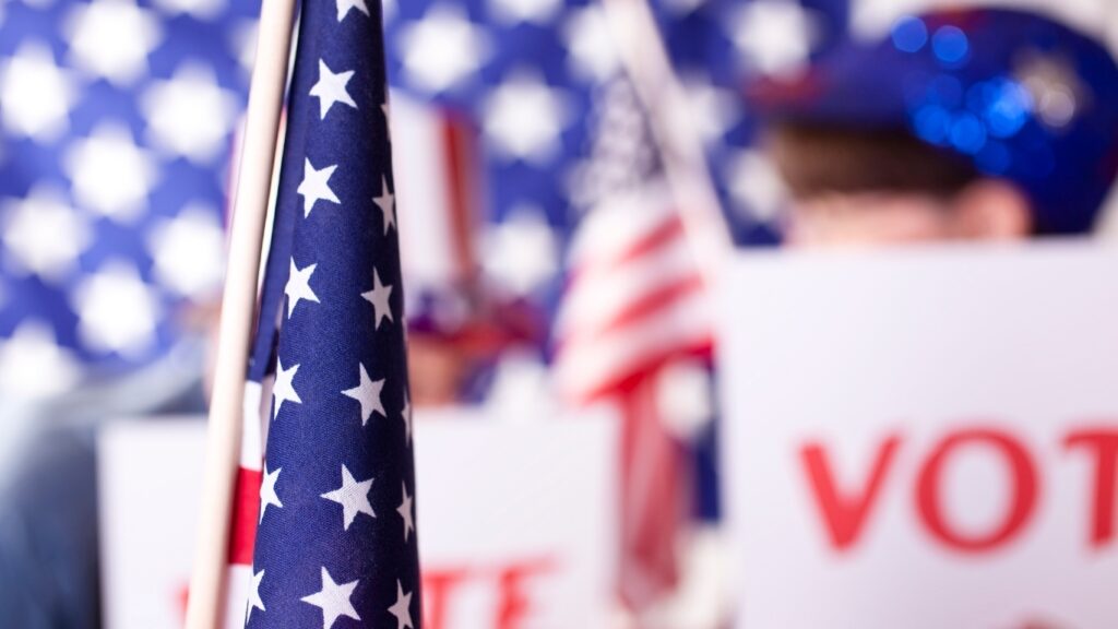 「VOTE」の看板が掲げられたアメリカの政治集会。アメリカ国旗。